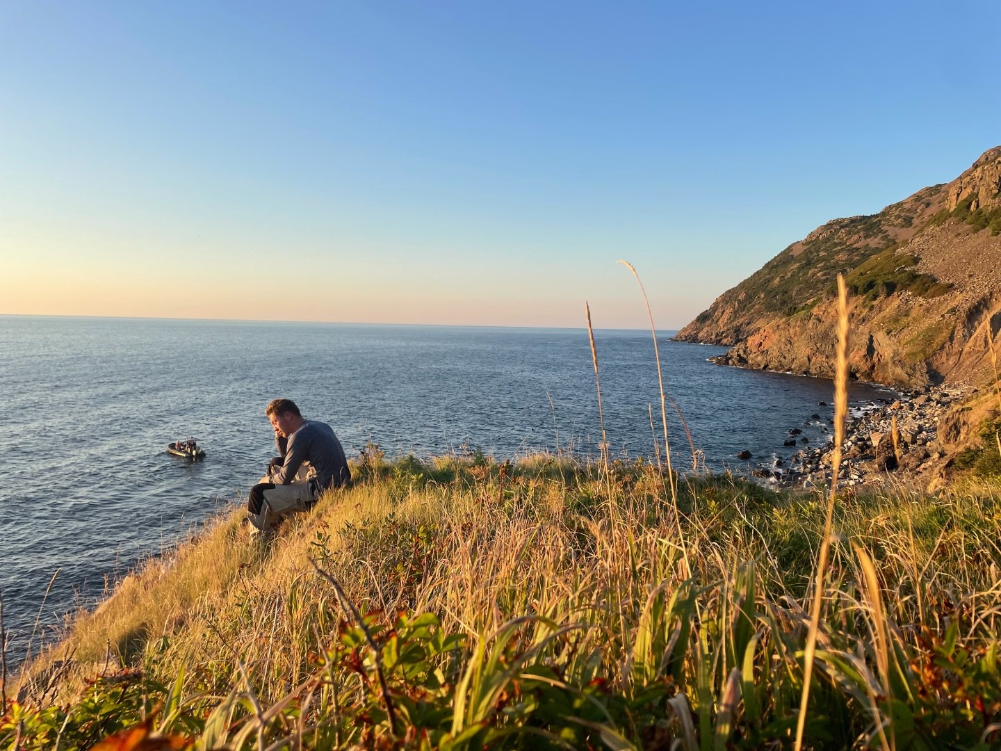 Golden-hour view from a clifftop over a quiet cove, a small boat on the water below