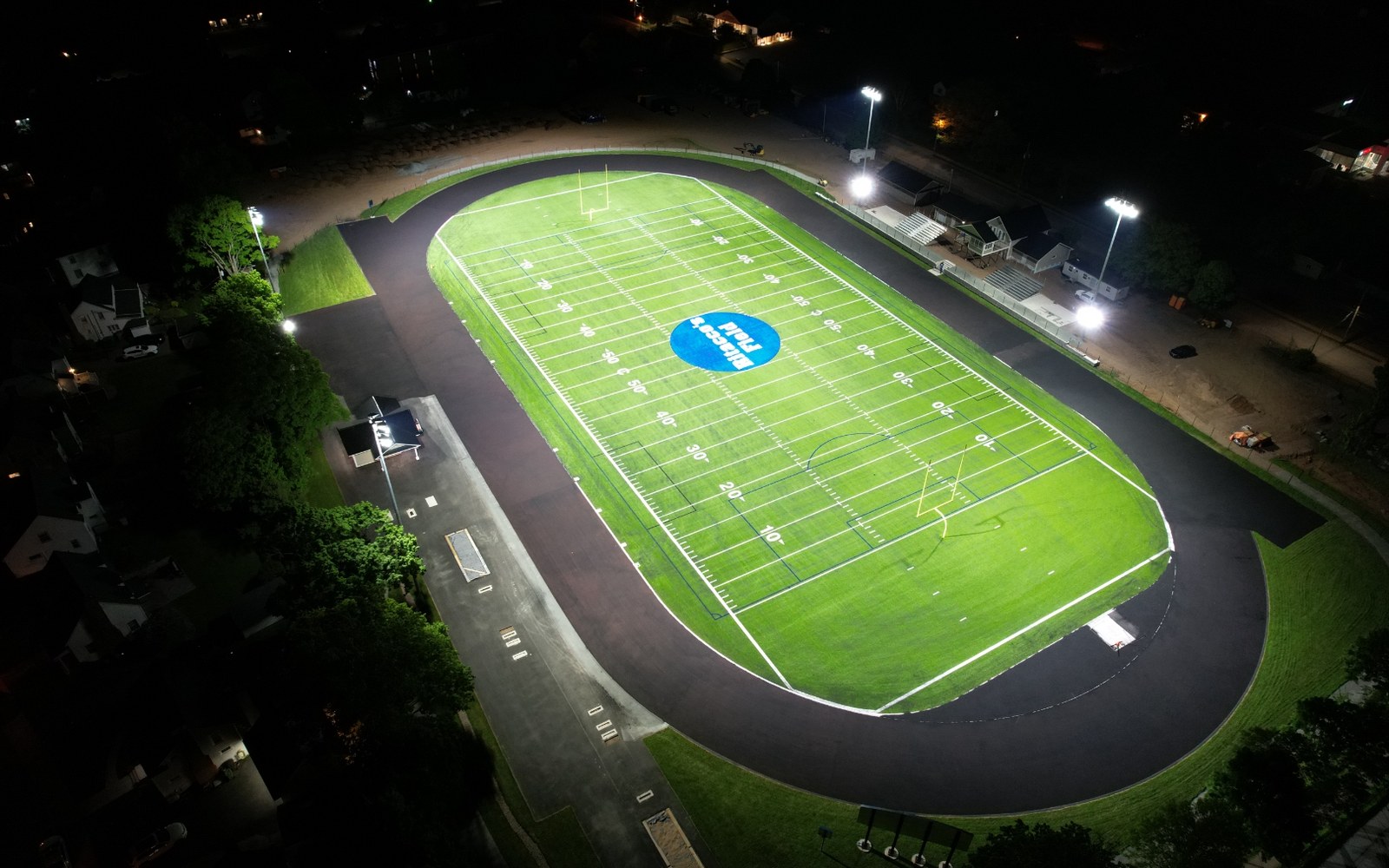 Night aerial of the floodlit turf field and track at the TAAC Grounds athletic park